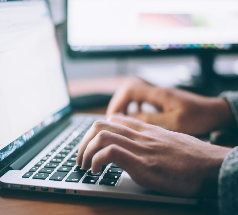 MasterClass Offerte Main en train de taper sur un ordinateur portable, avec un écran d'ordinateur en arrière-plan.
